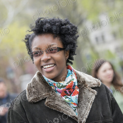 A group of people in a city park. A young woman in a coat with a large collar, smiling…