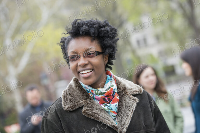 A group of people in a city park. A young woman in a coat with a large collar, smiling…