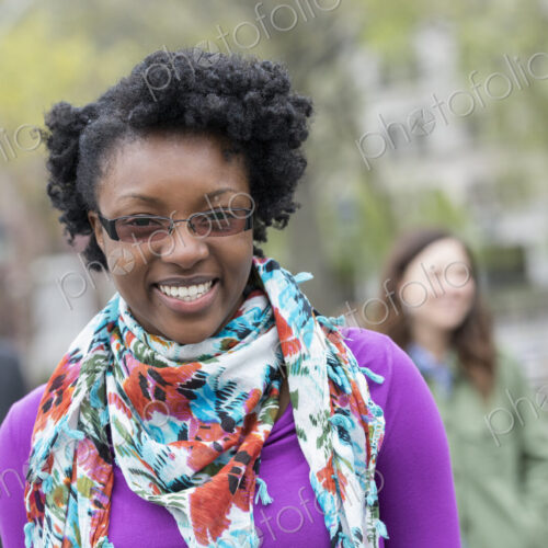 A group of people in a city park. A young woman smiling, wearing a purple shirt and…