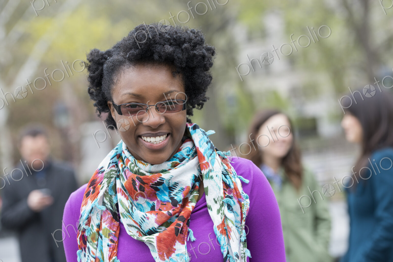 A group of people in a city park. A young woman smiling, wearing a purple shirt and…