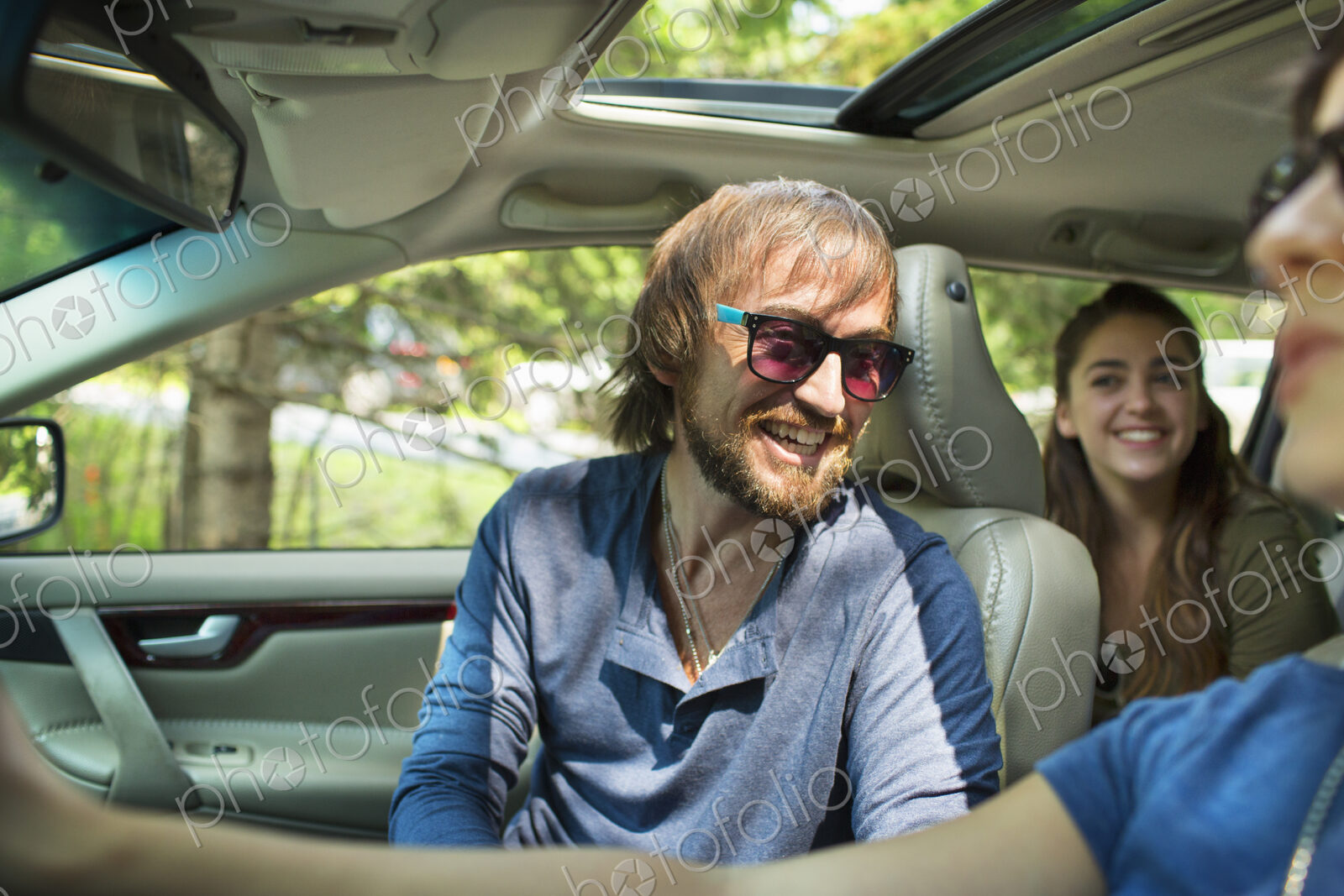 A group of people inside a car, on a road trip. A driver and two passengers.