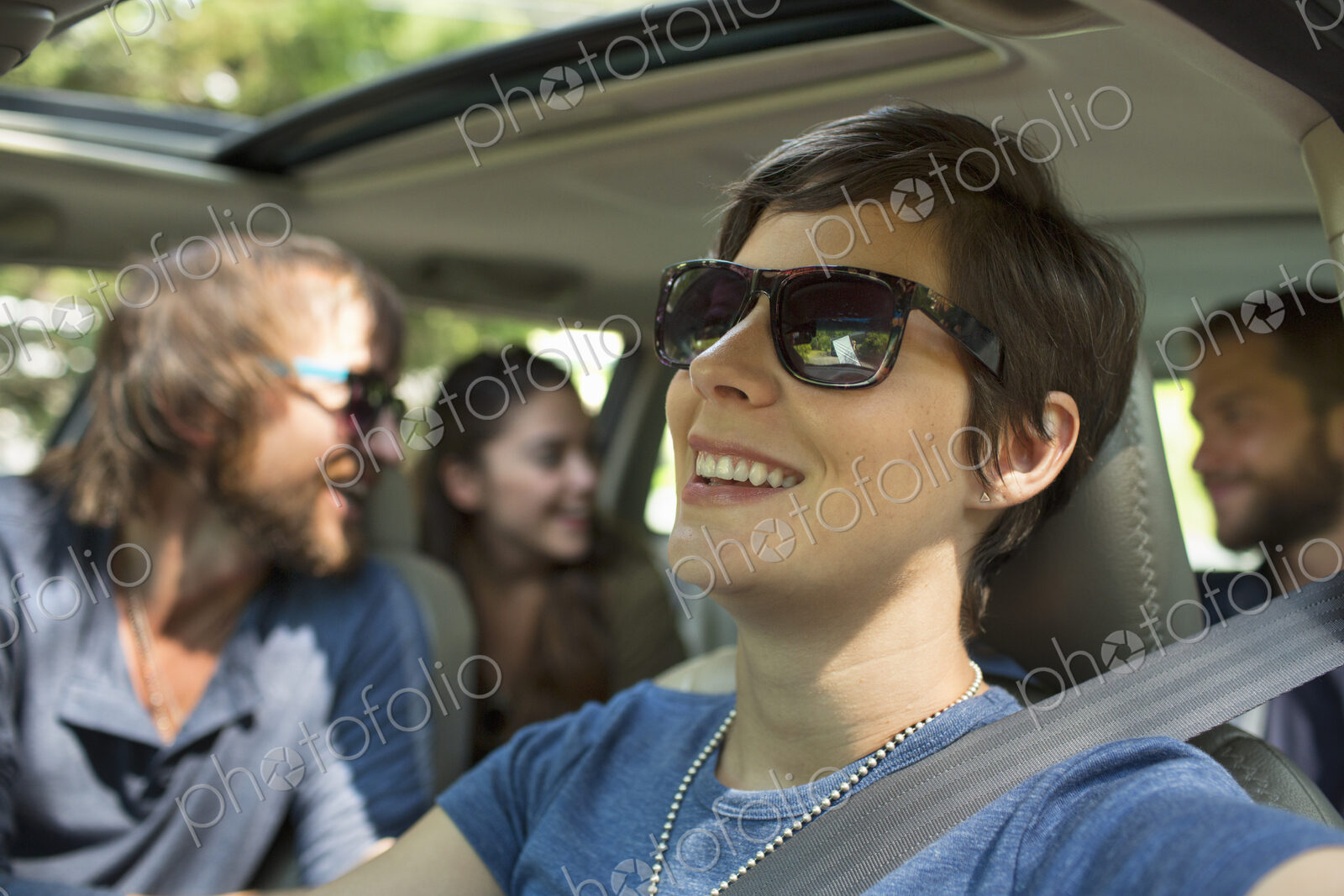 A group of people inside a car, on a road trip. View to the back seat, four passengers.