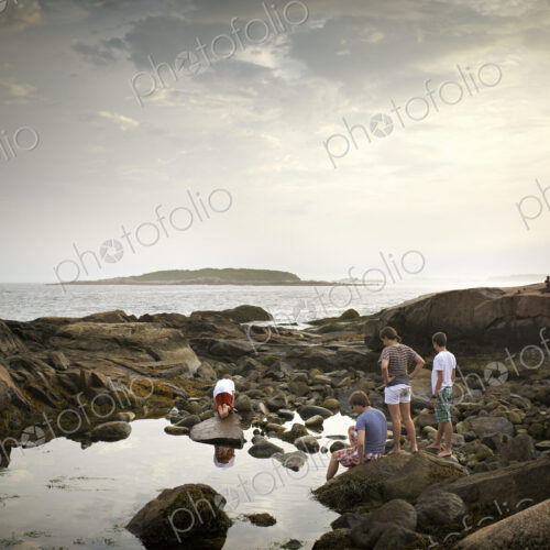 A group of people on the shore, rock pooling, and exploring the marine life. View to… A group of people on the shore, rock pooling, and exploring the marine life. View to…