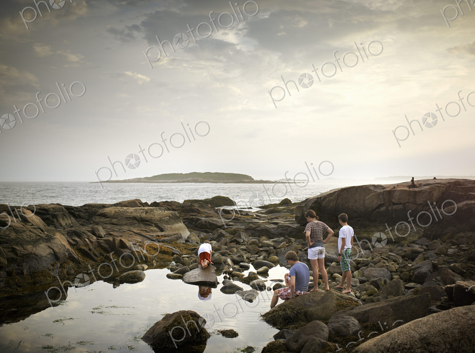 A group of people on the shore, rock pooling, and exploring the marine life. View to…