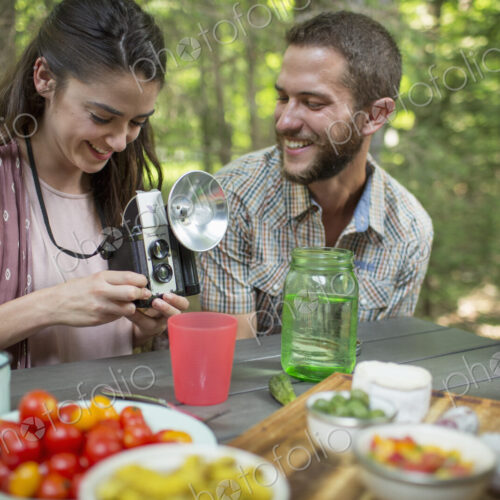 A group of people seated at a meal around a table outdoors. A couple side by side, one… A group of people seated at a meal around a table outdoors. A couple side by side, one…