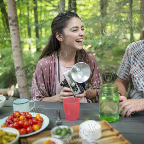 A group of people seated at a meal around a table outdoors. A couple side by side, one… A group of people seated at a meal around a table outdoors. A couple side by side, one…