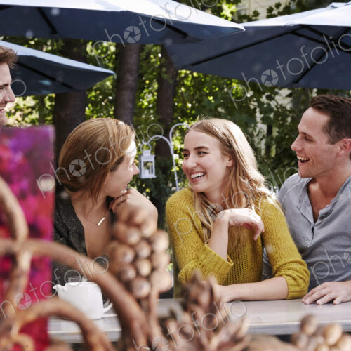A group of people sitting at a long table in an outdoor cafe. A group of people sitting at a long table in an outdoor cafe.