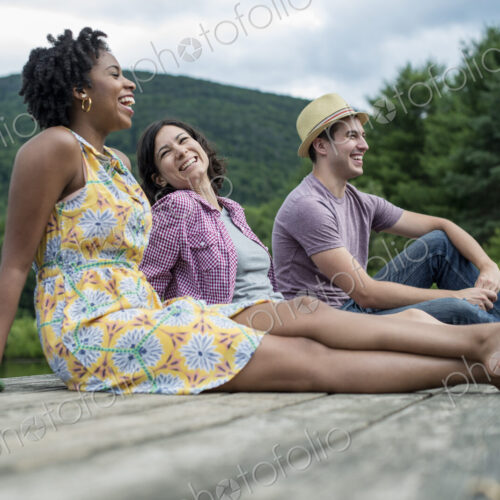 A group of people sitting on a woode pier overlooking a lake. A group of people sitting on a woode pier overlooking a lake.