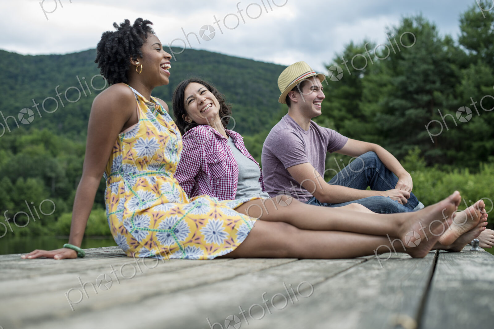 A group of people sitting on a woode pier overlooking a lake.