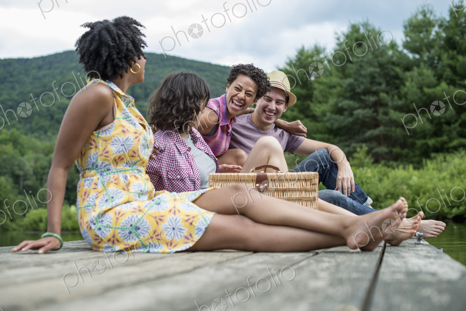 A group of people sitting on a woode pier overlooking a lake.