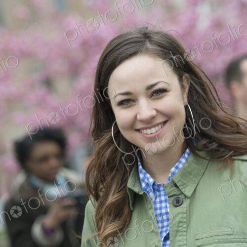A group of people under the cherry blossom trees in the park. A young woman in an open…