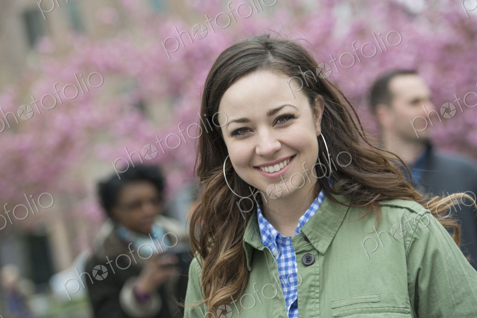 A group of people under the cherry blossom trees in the park. A young woman in an open…