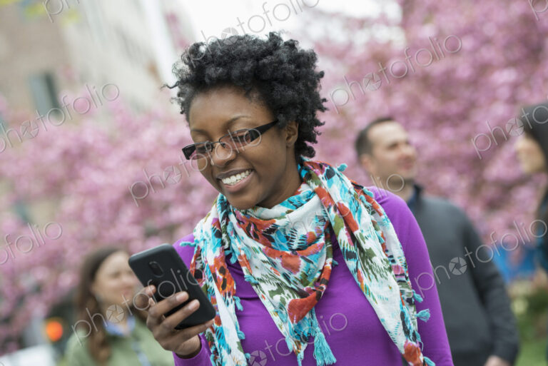 A group of people under the cherry blossom trees in the park. A young woman smiling…