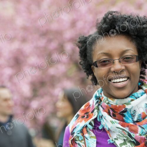 A group of people under the cherry blossom trees in the park. A young woman smiling…