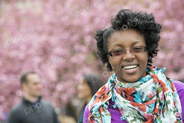 A group of people under the cherry blossom trees in the park. A young woman smiling…