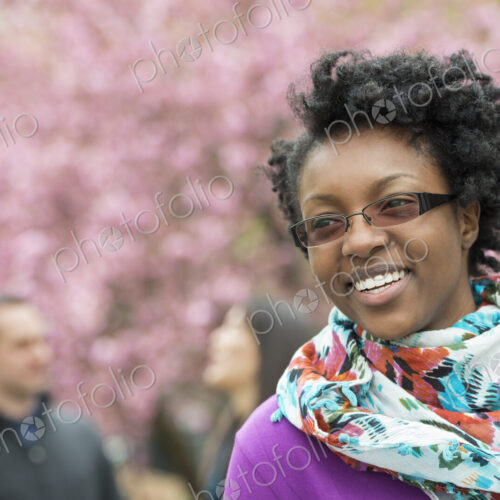 A group of people under the cherry blossom trees in the park. A young woman smiling,…