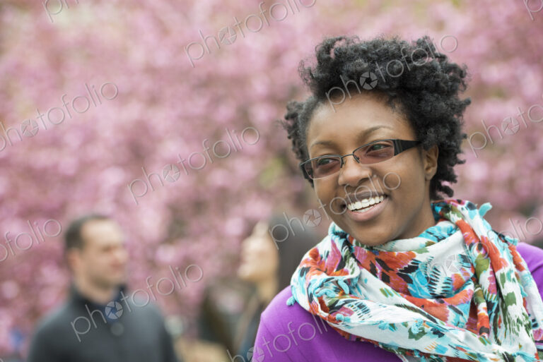 A group of people under the cherry blossom trees in the park. A young woman smiling,…