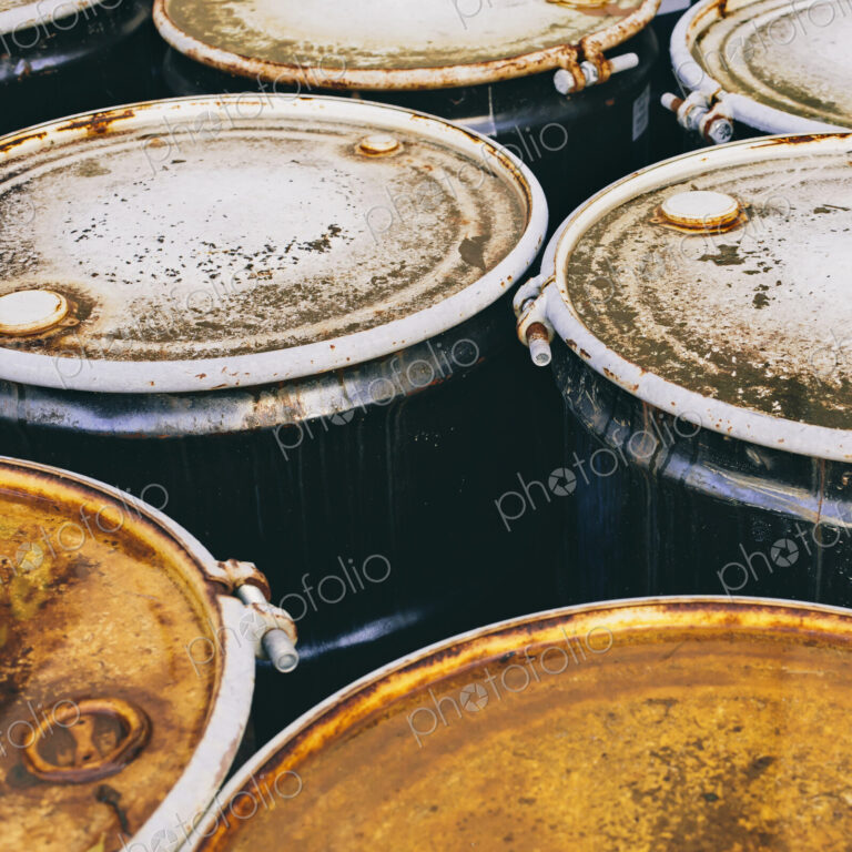 A group of rusted corroded barrels of chemical or petroleum products.