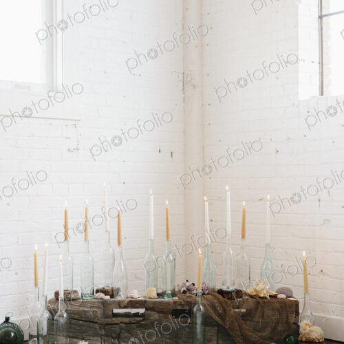 A group of tall lit candles in clear glass bottles arranged in a corner.