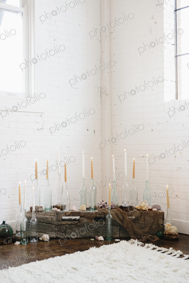 A group of tall lit candles in clear glass bottles arranged in a corner.