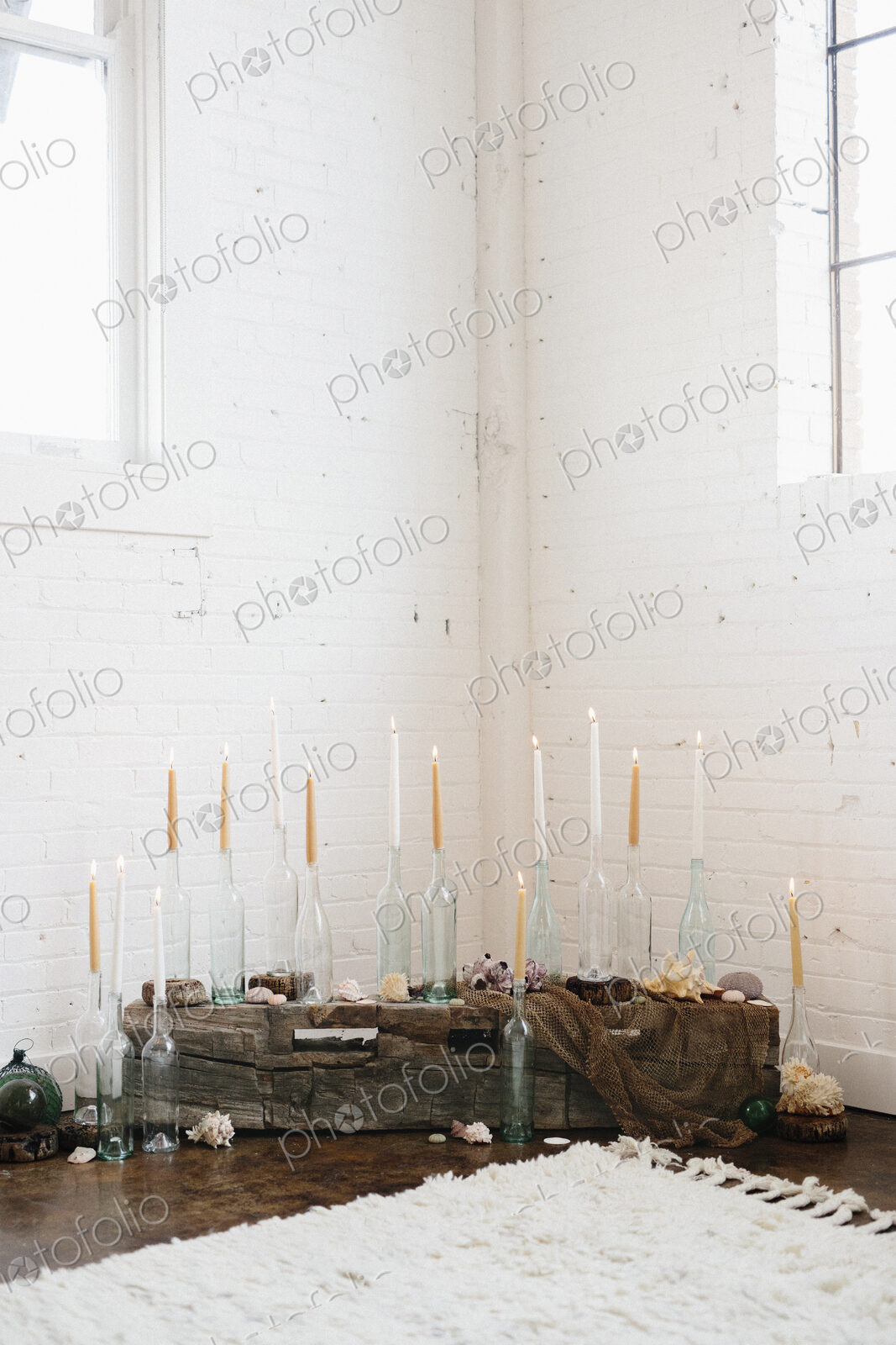A group of tall lit candles in clear glass bottles arranged in a corner.