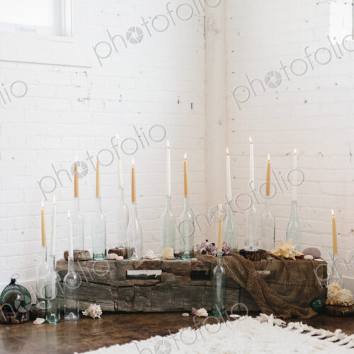 A group of tall lit candles in clear glass bottles arranged in a corner.