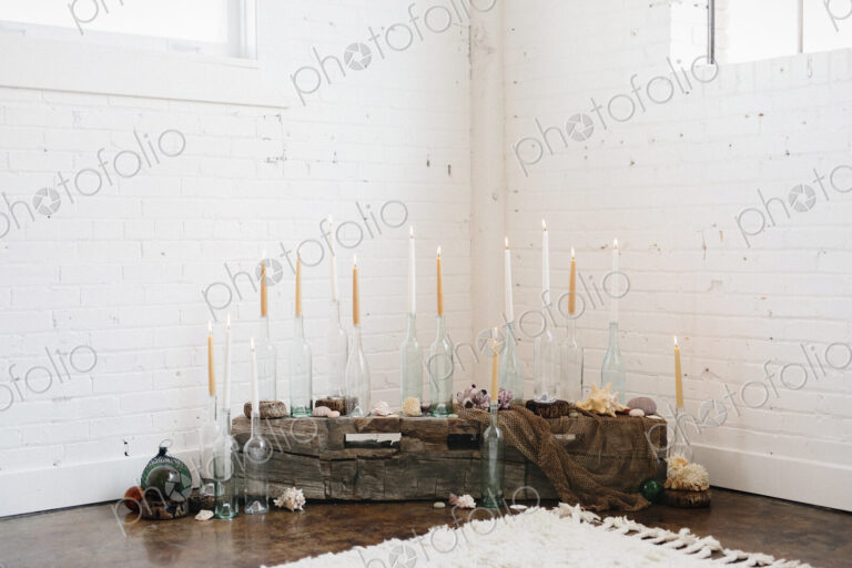 A group of tall lit candles in clear glass bottles arranged in a corner.