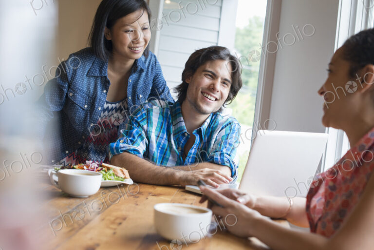 A group of three people in a cafe. Sharing a laptop and using smart phones.