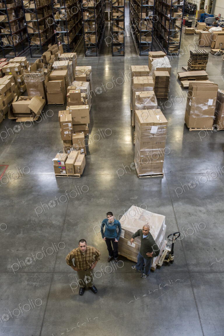 A group of three warehouse workers standing in the center of a distirbution warehouse.