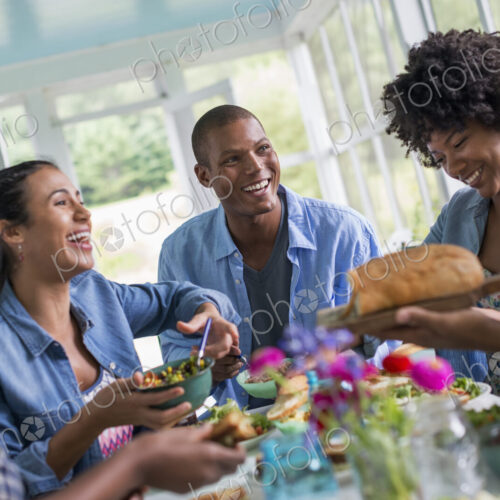 A group of women and men around a table sharing a meal in a farmhouse kitchen. A group of women and men around a table sharing a meal in a farmhouse kitchen.