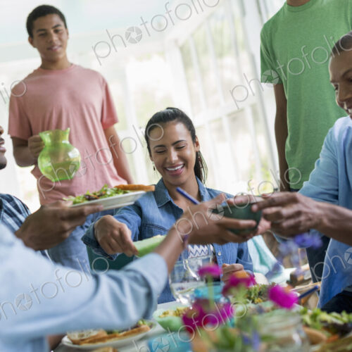 A group of women and men around a table sharing a meal in a farmhouse kitchen.