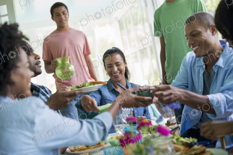 A group of women and men around a table sharing a meal in a farmhouse kitchen.
