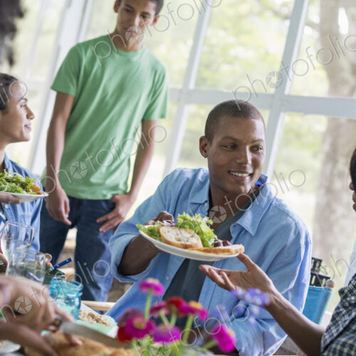 A group of women and men around a table sharing a meal in a farmhouse kitchen. A group of women and men around a table sharing a meal in a farmhouse kitchen.