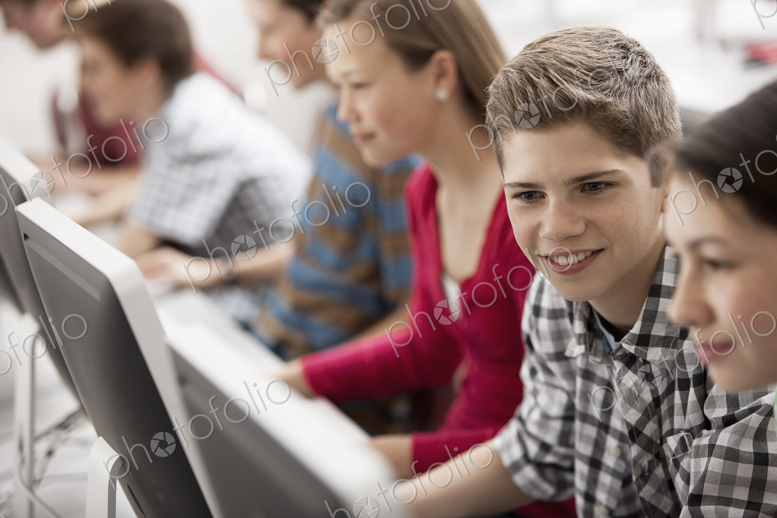 A group of young people, boys and girls, working at computer screens in class.