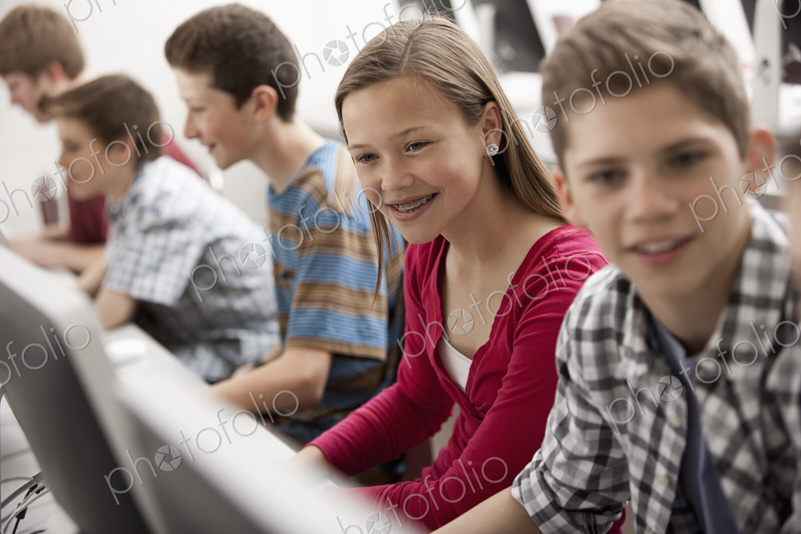 A group of young people, boys and girls, working at computer screens in class.