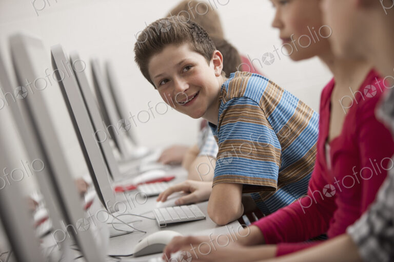 A group of young people, boys and girls, working at computer screens in class.
