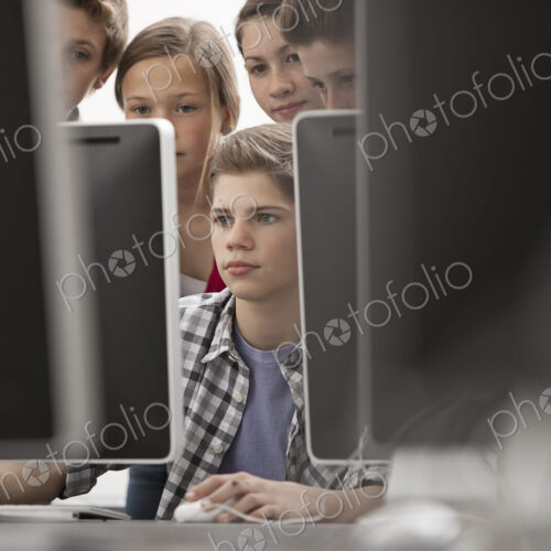 A group of young people, boys and girls, working at computer screens in class.