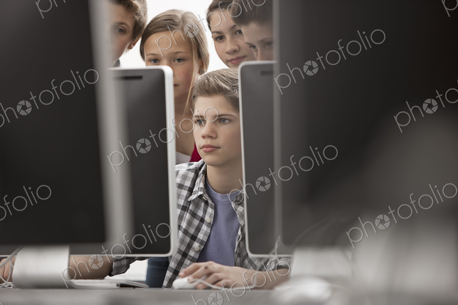 A group of young people, boys and girls, working at computer screens in class.