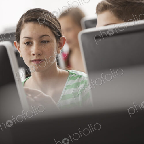 A group of young people, boys and girls, working at computer screens in class.