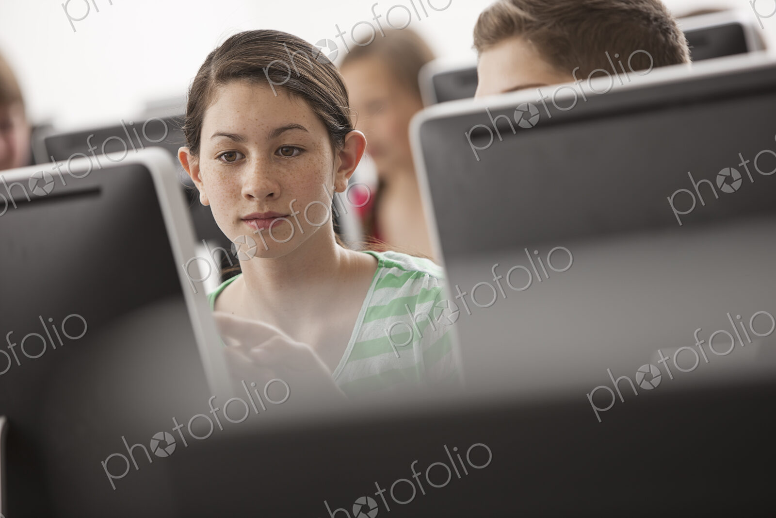A group of young people, boys and girls, working at computer screens in class.