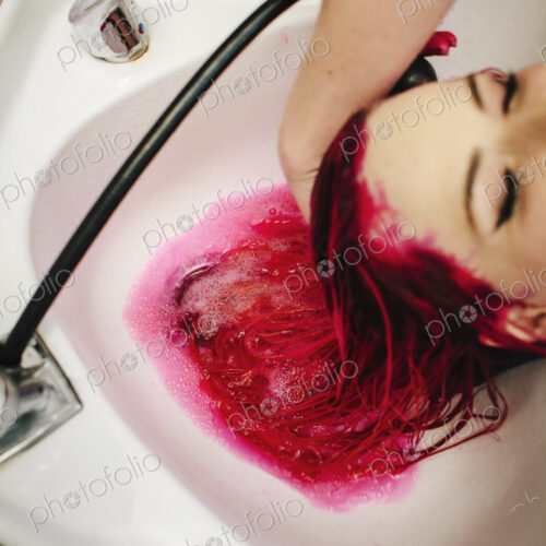 A hair salon cleint having red hair dye rinsed from her hair over a basin. A hair salon cleint having red hair dye rinsed from her hair over a basin.