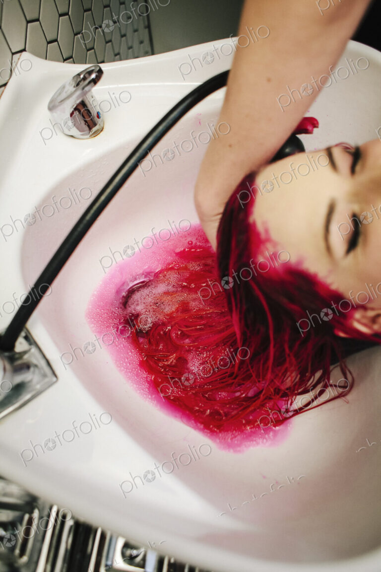A hair salon cleint having red hair dye rinsed from her hair over a basin.