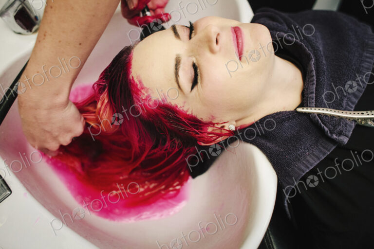 A hair salon client having red hair dye rinsed from her hair over a basin.