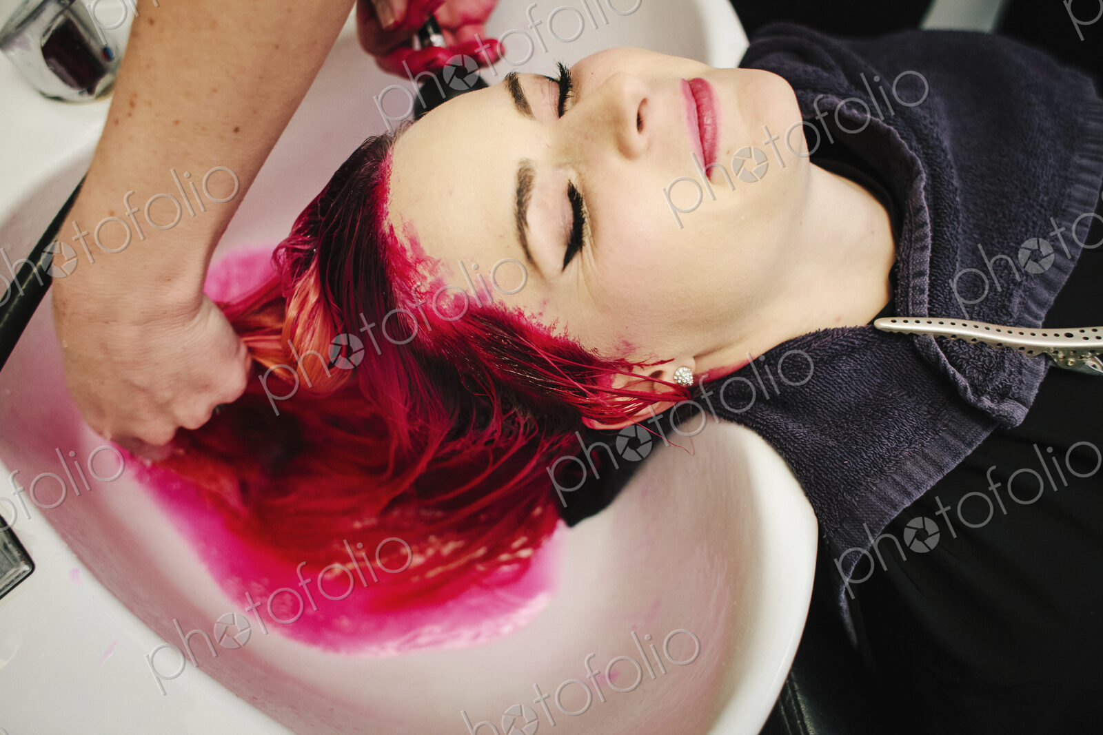 A hair salon client having red hair dye rinsed from her hair over a basin.