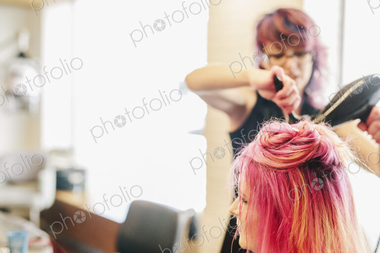 A hair stylist blowdrying a client's long pink dyed hair.