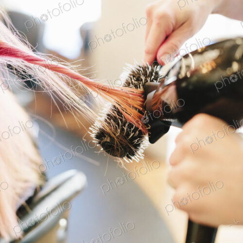 A hair stylist blowdrying a client's long straight pink hair using a round bristle brush. A hair stylist blowdrying a client's long straight pink hair using a round bristle brush.