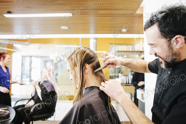 A hair stylist with a client, combing her long hair in sections.