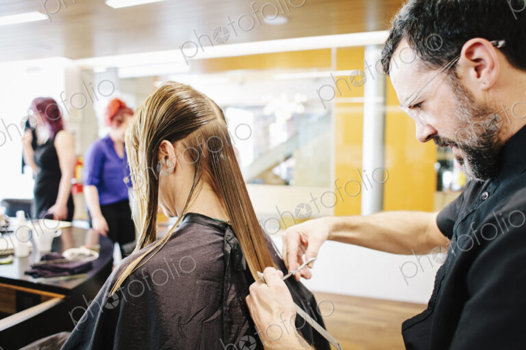 A hair stylist with a client, cutting her long straight hair.