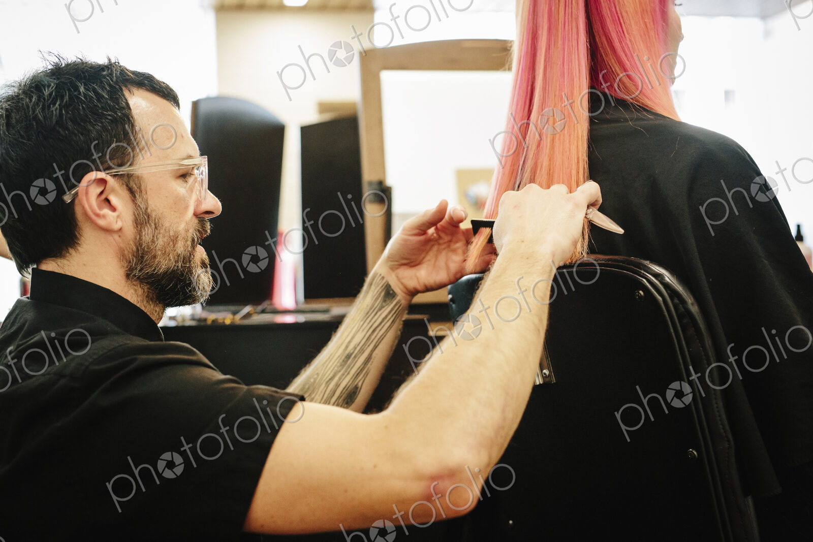 A hair stylist with a client, cutting her long straight hair, trimming the ends.