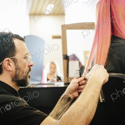 A hair stylist with a client, trimming the ends of her long dyed pink straight hair. A hair stylist with a client, trimming the ends of her long dyed pink straight hair.